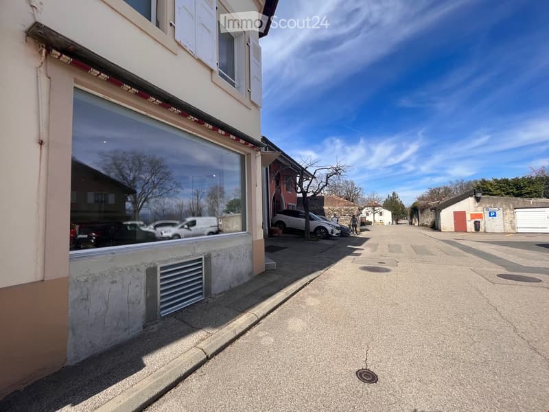 Building with a glass storefront, white shutters, and a garage with cars parked in front.