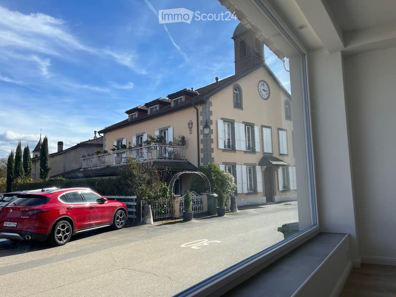 large building, beige exterior, clock, balcony, red car parked in front