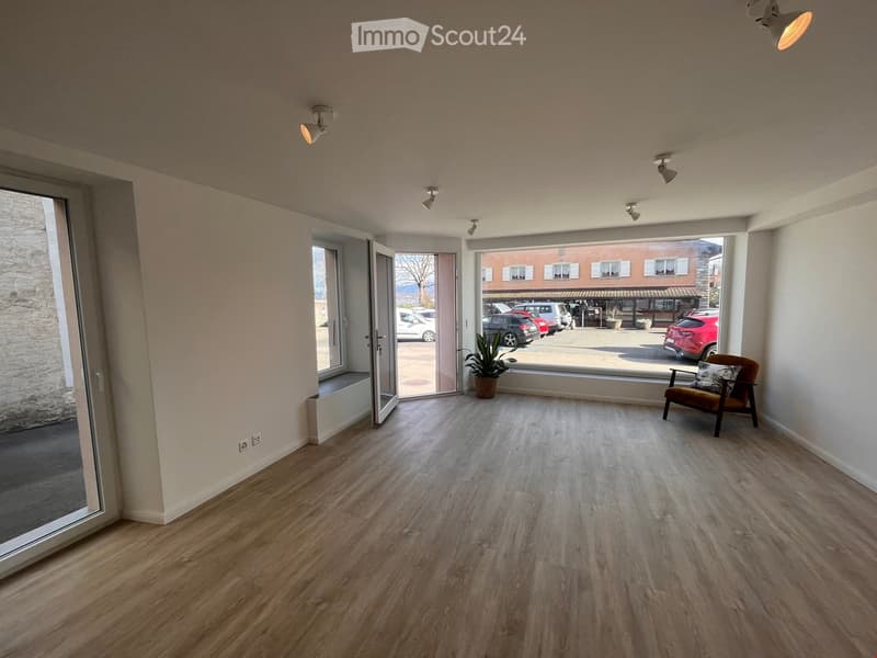 large room, wooden floor, white walls, large windows, plants, chair, open doors