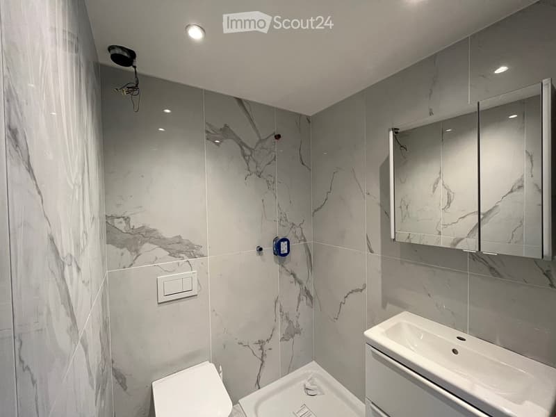 modern bathroom with white marble tiles, white sink, white toilet, shower area, mirror