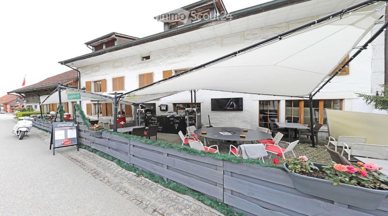 white building, outdoor seating area, large canopy, tables and chairs, potted plants, television