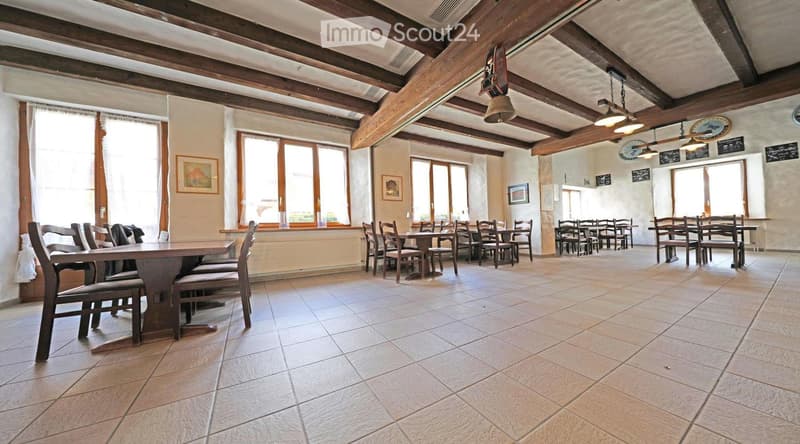 large room, wooden beams, tiled floor, wooden tables and chairs, windows, picture frames