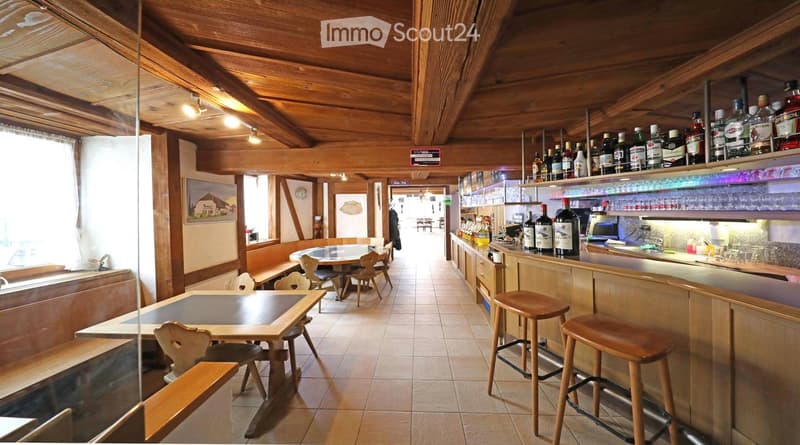 wooden ceiling, wooden tables and chairs, bar counter, bottles of alcohol, tiled floor