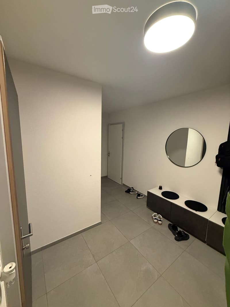 Empty room with white walls, tiled floor, round mirror, and a shoe rack with shoes