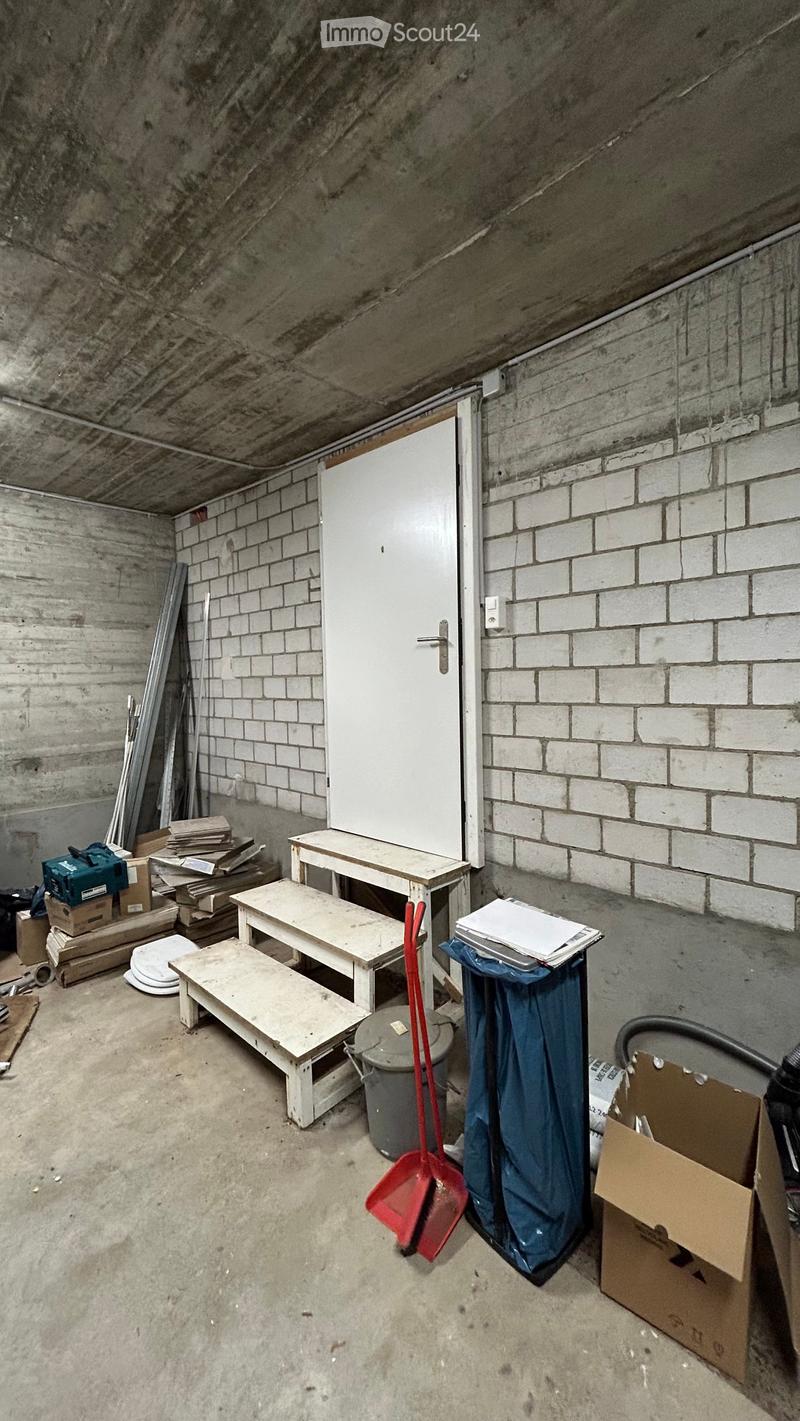 Storage room with a white door, brick walls, concrete floor, storage boxes, buckets, and cleaning tools