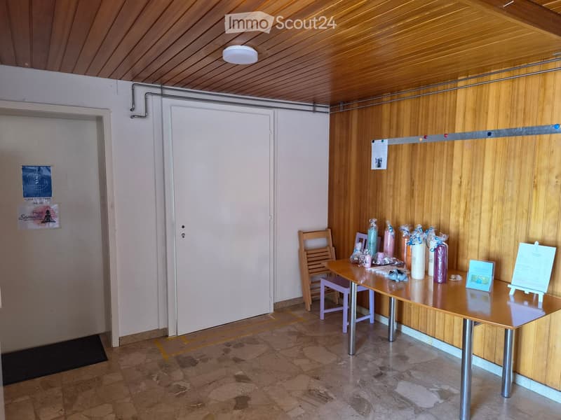 Empty room with wooden walls, tiled floor, white door, table with items, and a small rug