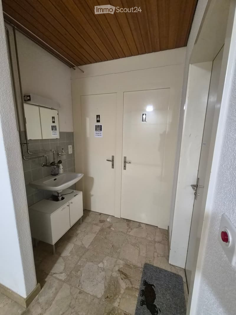 Small bathroom with sink, mirror, and cabinets, tiled floor, white walls, and a door.