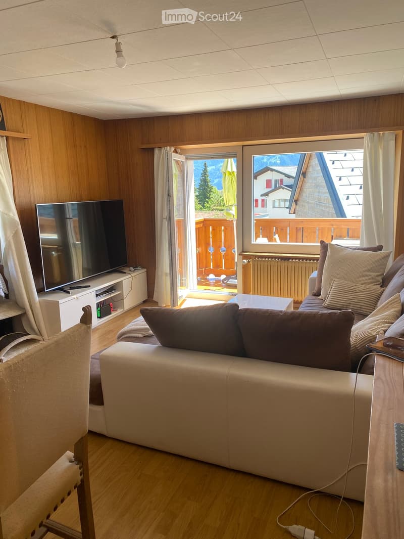 Modern living room with a large window offering a scenic mountain view, a comfortable sofa, a coffee table, a TV stand, and a chair.