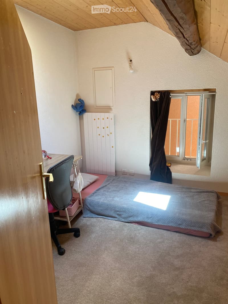 Cozy bedroom with a single bed, desk, chair, wardrobe, and a small window with a view to a balcony.