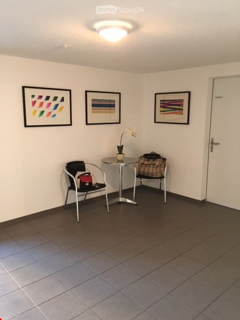 Empty room with two chairs, a table, a flower vase, and three paintings on the wall