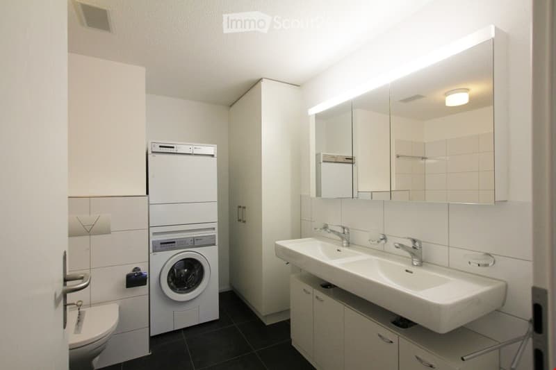 modern bathroom with white tiles, white sink, white toilet, washing machine, mirror, and cabinets