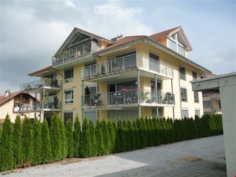 2 story apartment building, yellow exterior, multiple balconies, red roof, hedges in front