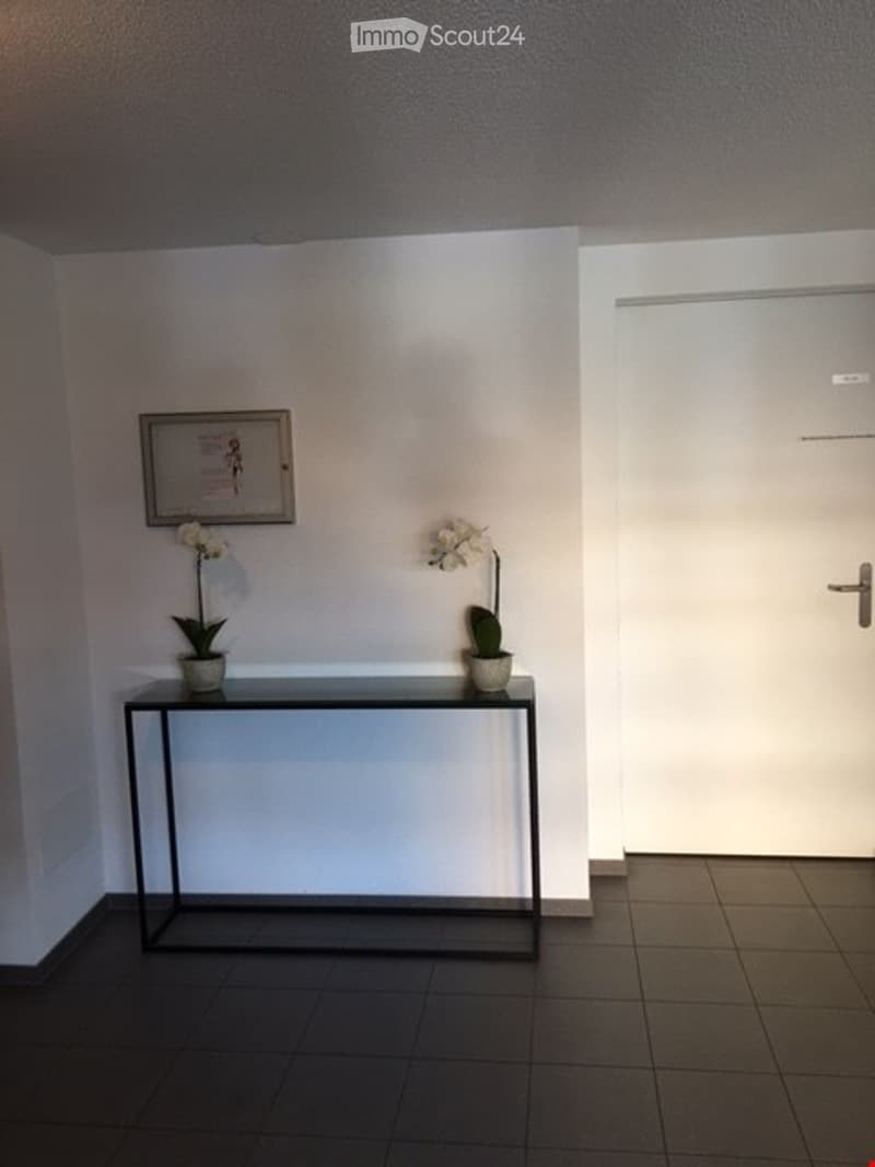 Empty room with white walls, black floor, a table with two flower pots, and a picture frame on the wall.