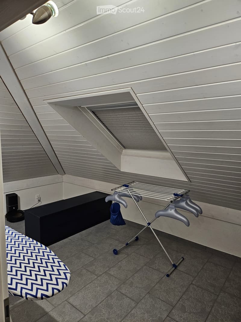 Laundry area with ironing board, clothes rack, black cabinet, and speaker mounted on the wall.
