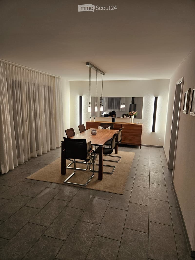 Dining room, wooden table, 6 chairs, beige carpet, tiled floor, wooden sideboard, large mirror, white curtains, decorative lights