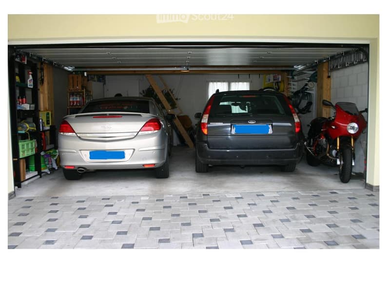 Garage with two cars and a motorcycle parked, storage shelves, brick walls, tiled floor