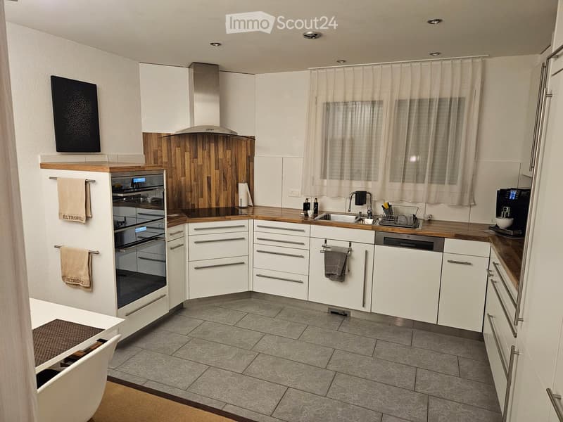 modern kitchen with white cabinets, gray tiled floor, wooden countertops, integrated oven and dishwasher, kitchen island with sink and faucet, white walls, white ceiling, window with white curtains