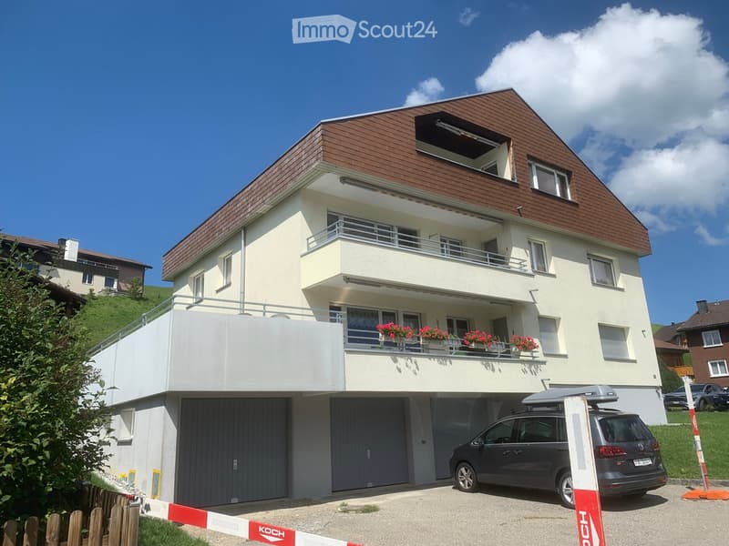 2 story house, white walls, brown roof, balcony with flowers, 2 garages, car parked in front
