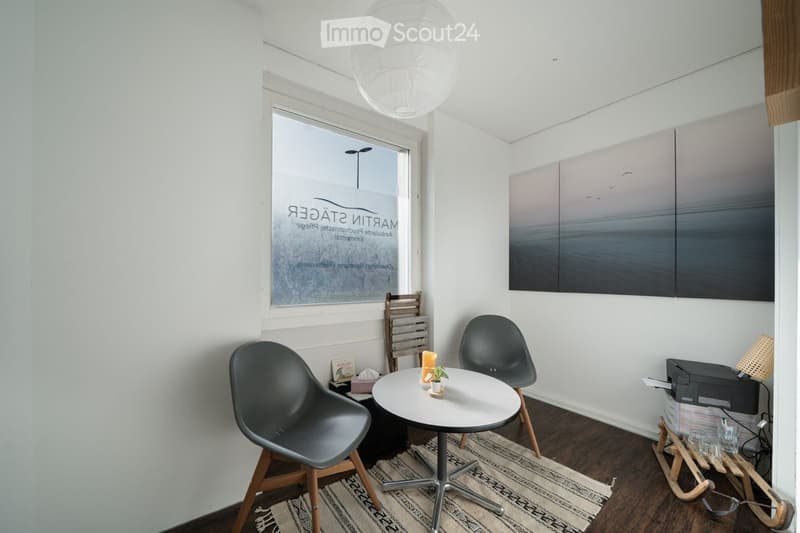 small room with white walls, wooden floor, round table, two chairs, lamp, window, artwork, printer