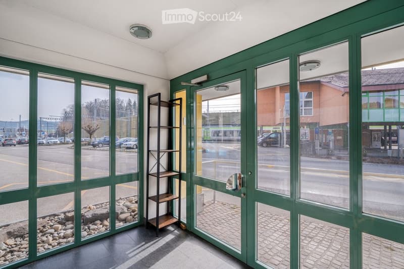 Entrance hall with green glass walls, tiled floor, small shelf, and a view of the street outside