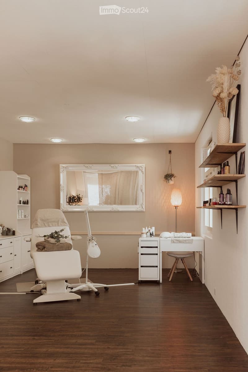 A room with a white chair, a desk, a mirror, and shelves with bottles and a plant