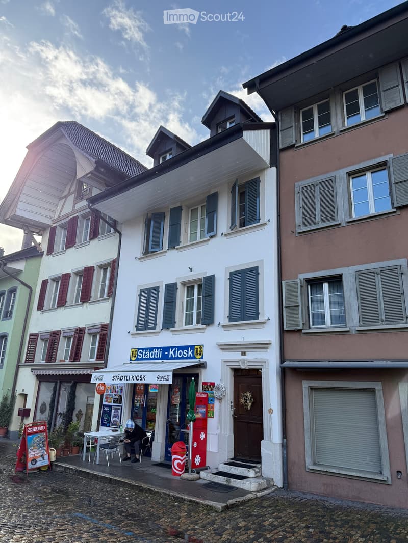 3 story building, white exterior, red shutters, storefront with awning, steps leading to entrance, outdoor seating area