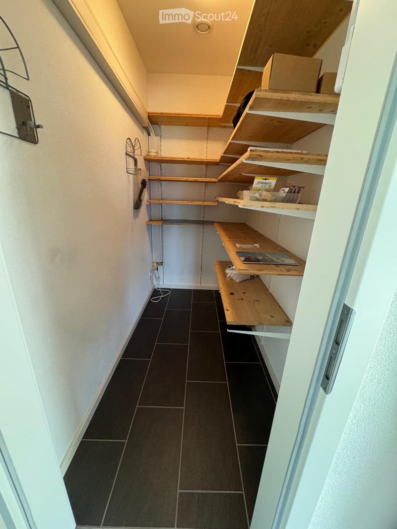 Storage room with wooden shelves, black tiled floor, white walls, hanging items, power outlet, boxes, and a bag on the shelves.