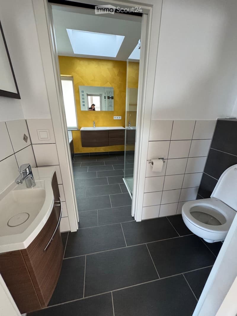Bathroom with yellow wall, black tiles, white sink, white toilet, mirror, and a glass shower enclosure