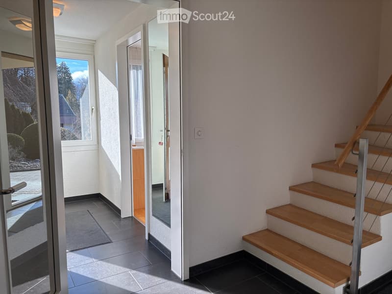 Entrance hall with wooden stairs, white walls, black tiles, glass door, mirror, window