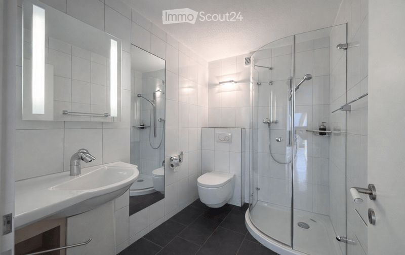 modern bathroom with white tiles, glass shower, white sink, toilet, mirror, and towel rack