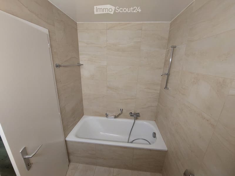 Bathroom with bathtub, tiled walls, and a white door.
