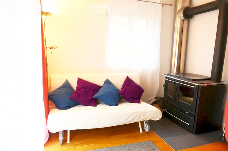 Cozy living room with a white sofa, colorful pillows, a wood stove, and a floor lamp near large windows with sheer curtains.