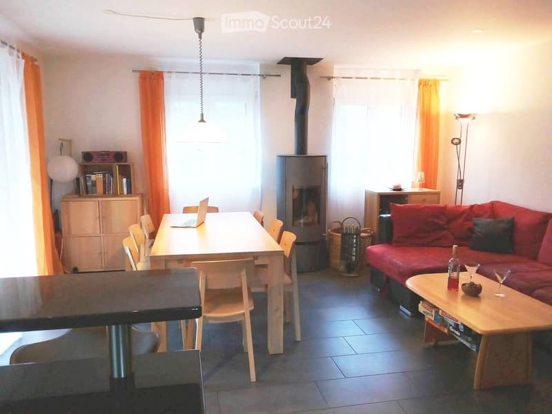 Bright living room with a red sofa, coffee table, dining table, chairs, laptop, bookshelf, and fireplace.