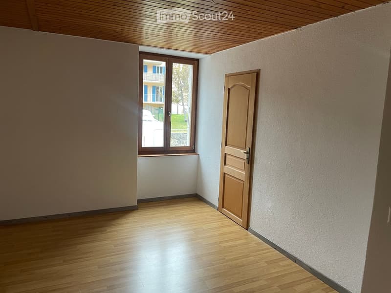 Wooden floor, white walls, wooden door, single window with view of an outside area