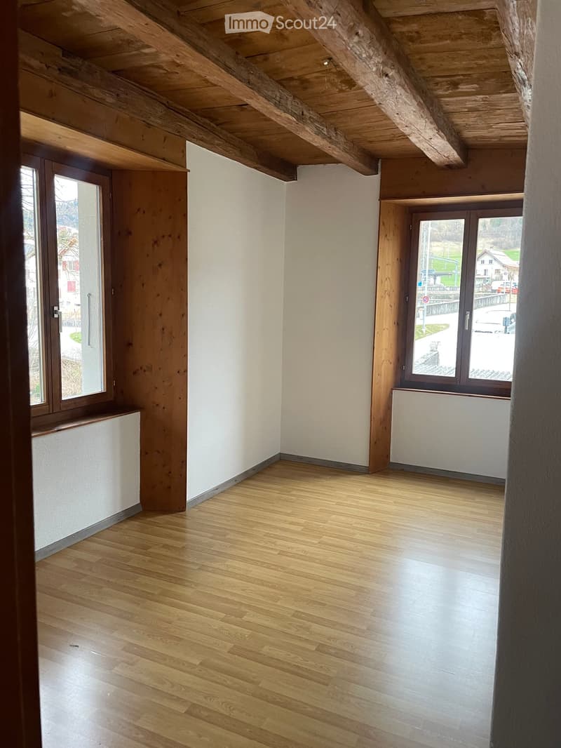 Empty room with wooden floor, wooden beam ceiling, two windows, white wall