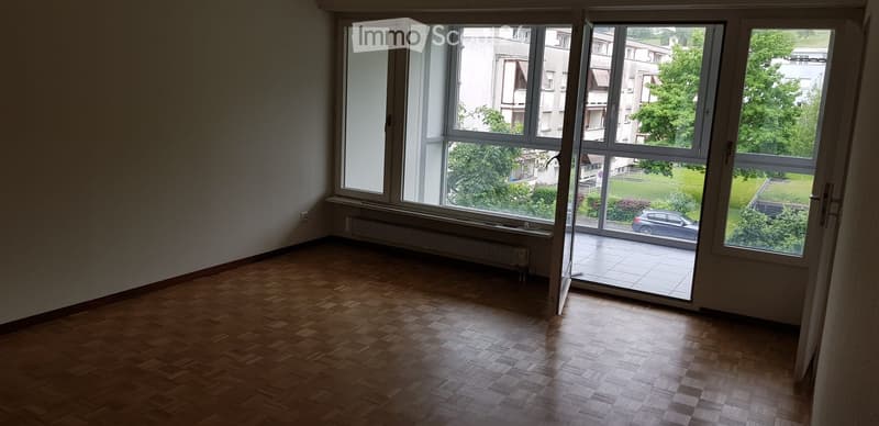 empty room, wooden floor, large windows, balcony, view of trees and buildings