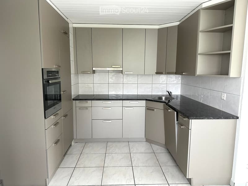 modern kitchen with white tiles, gray cabinets, black countertops, built-in oven and dishwasher