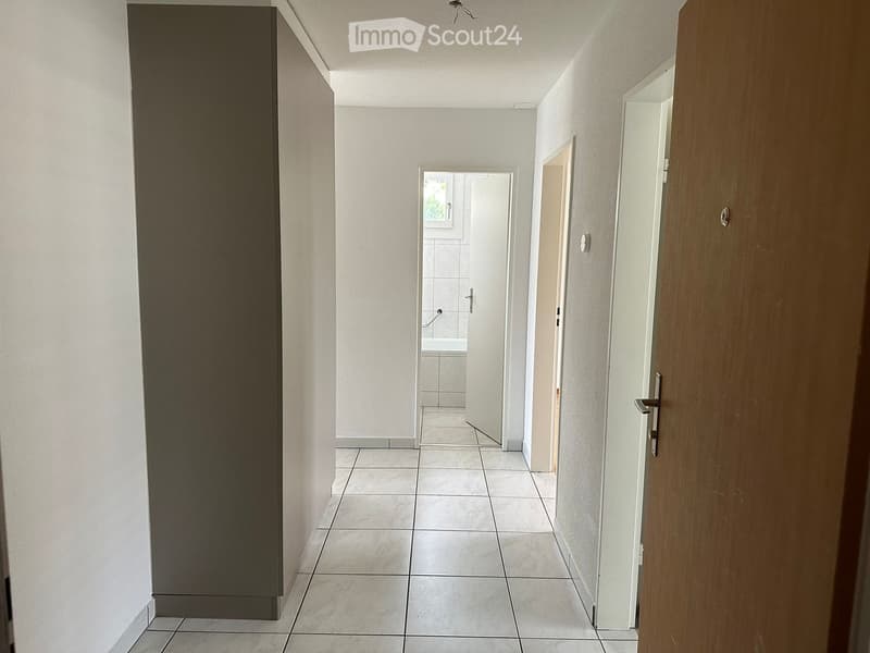 Empty hallway with white tiles, white walls, and a wooden door.