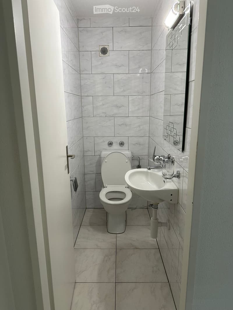 small bathroom with white tiles, toilet, sink, mirror, and light