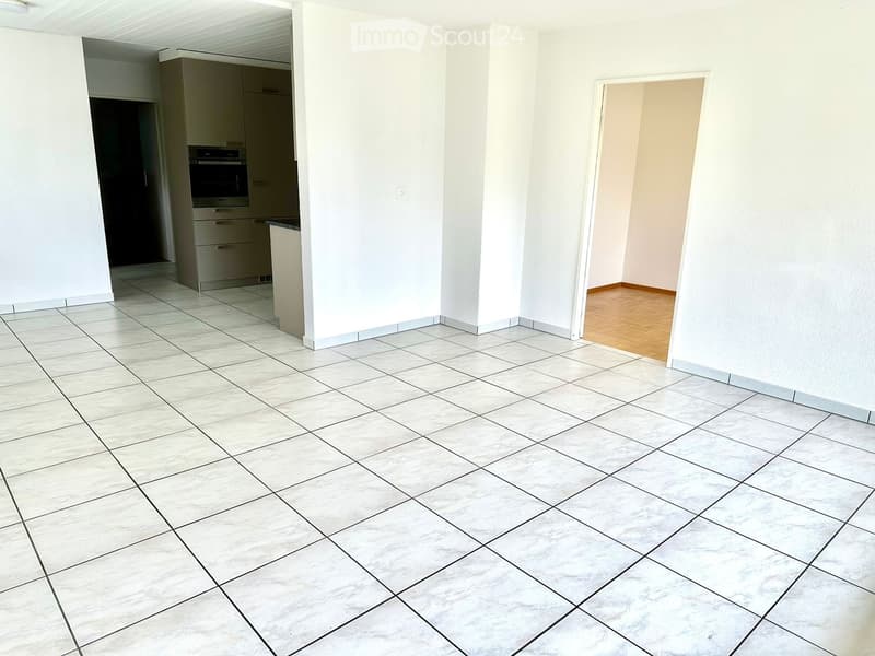 empty room, white tiles, white walls, wooden floor in the hallway, kitchen area with cabinets and oven