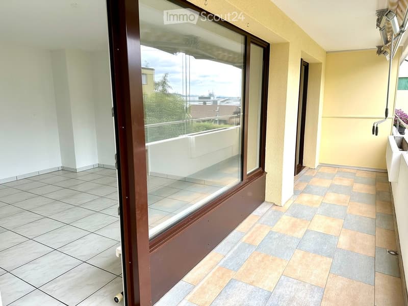 Balcony with glass door, tiled floor, white walls, view of the city