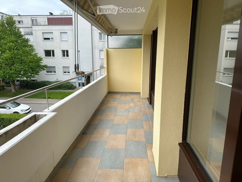 Balcony with tiled floor, metal railing, and a view of the street and a building