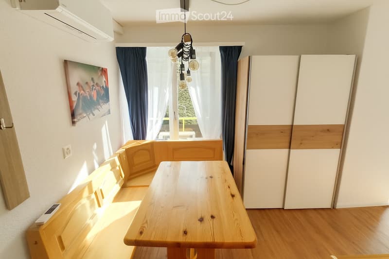 Dining area with wooden table, wooden bench, white walls, white cabinets, white curtains, picture frame, air conditioner