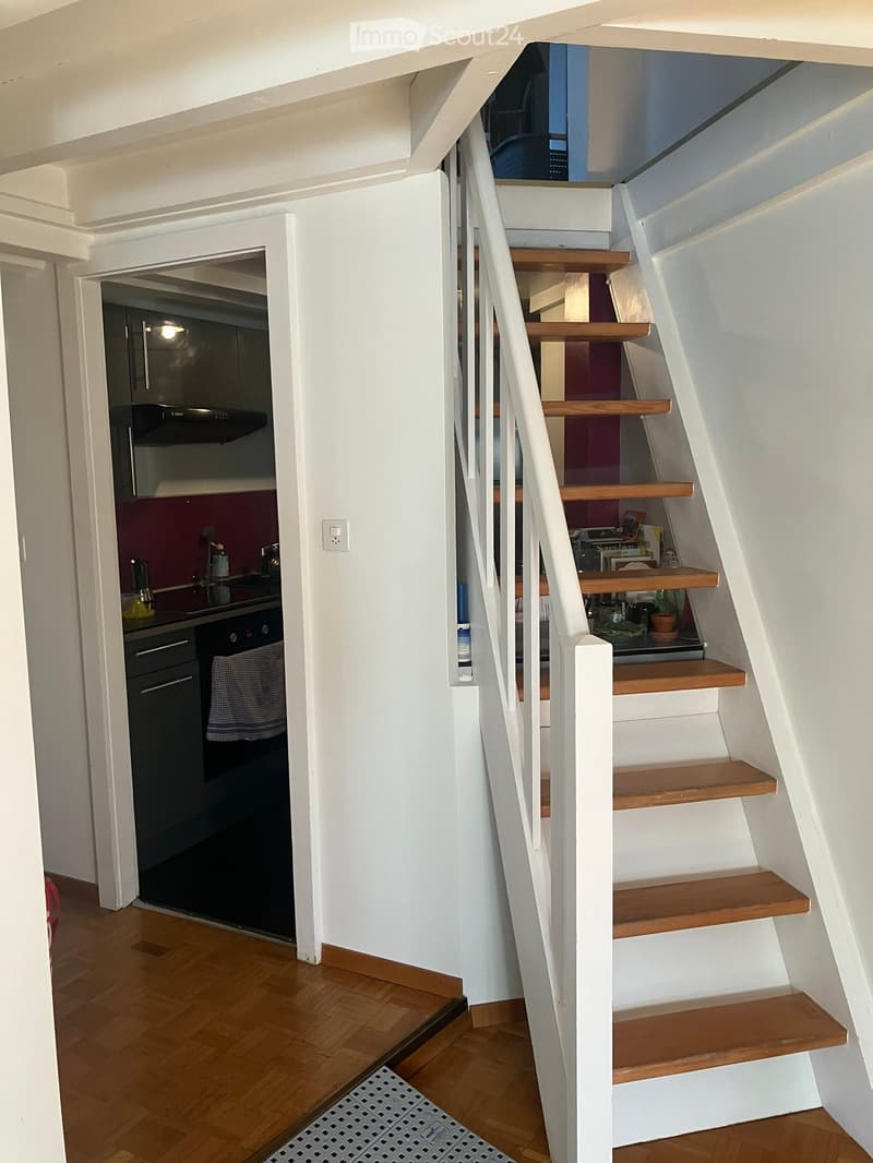 white walls, wooden floor, white staircase, kitchen with black appliances, open door to another room