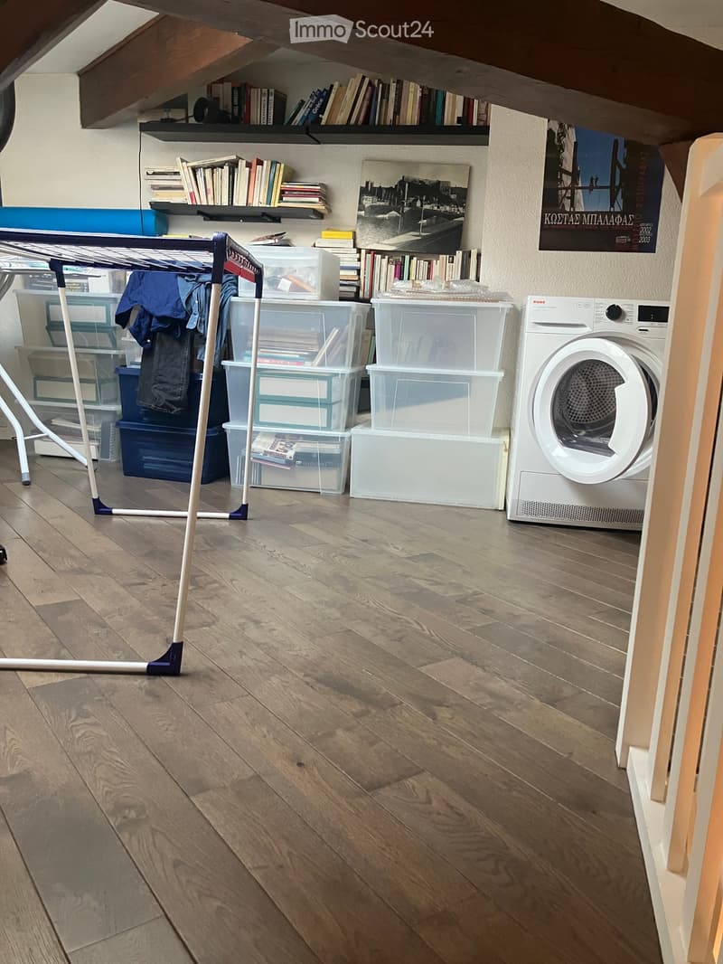 wooden floor, white walls, shelves with books, storage boxes, clothes on a hanger, washing machine