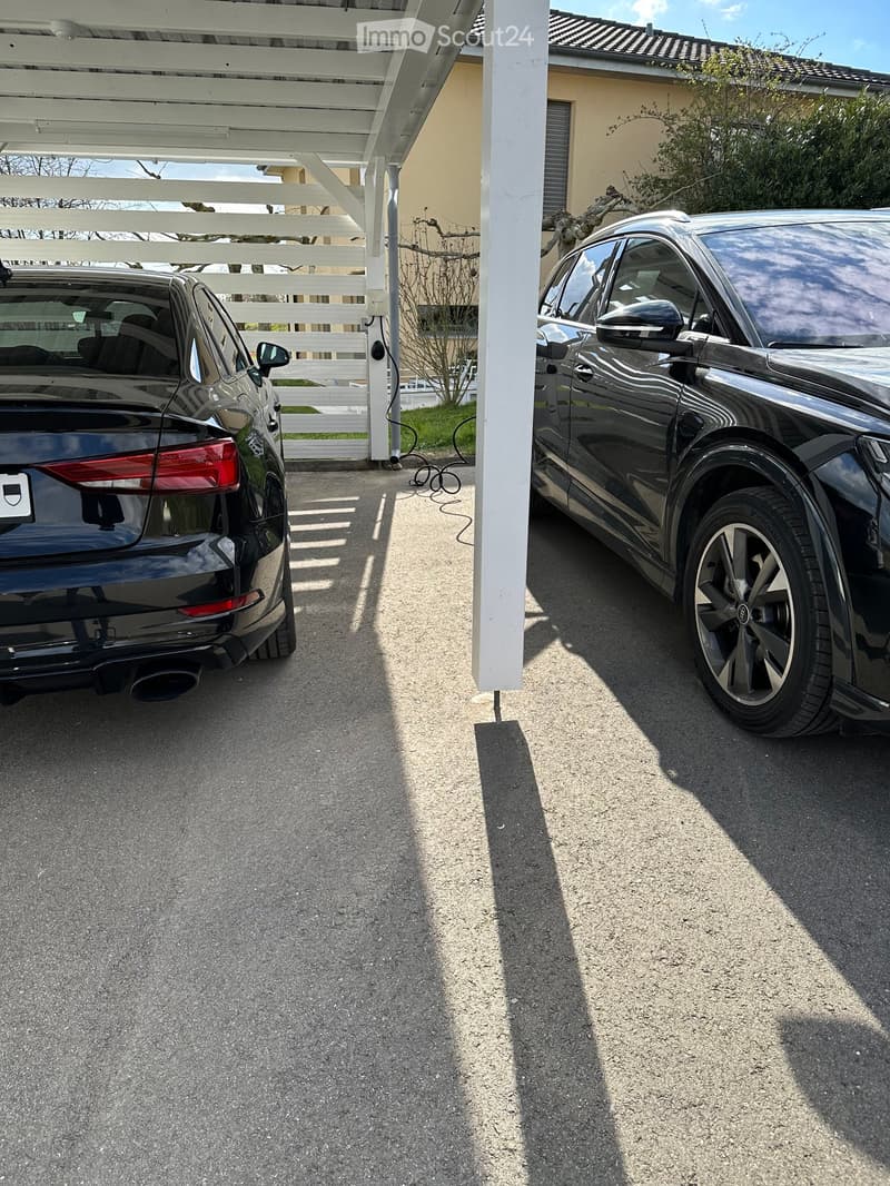 Two black cars parked under a carport, one with a charging cable connected