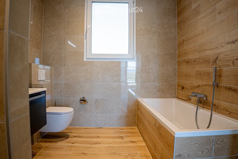 Bathroom with wooden floor, beige tiles, white bathtub, white toilet, white sink, window
