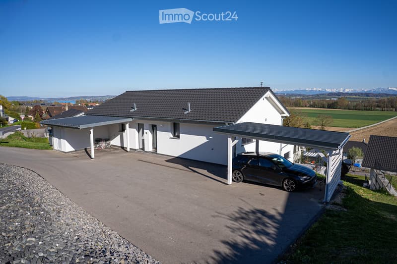 white house, black roof, car parked under carport, gravel driveway