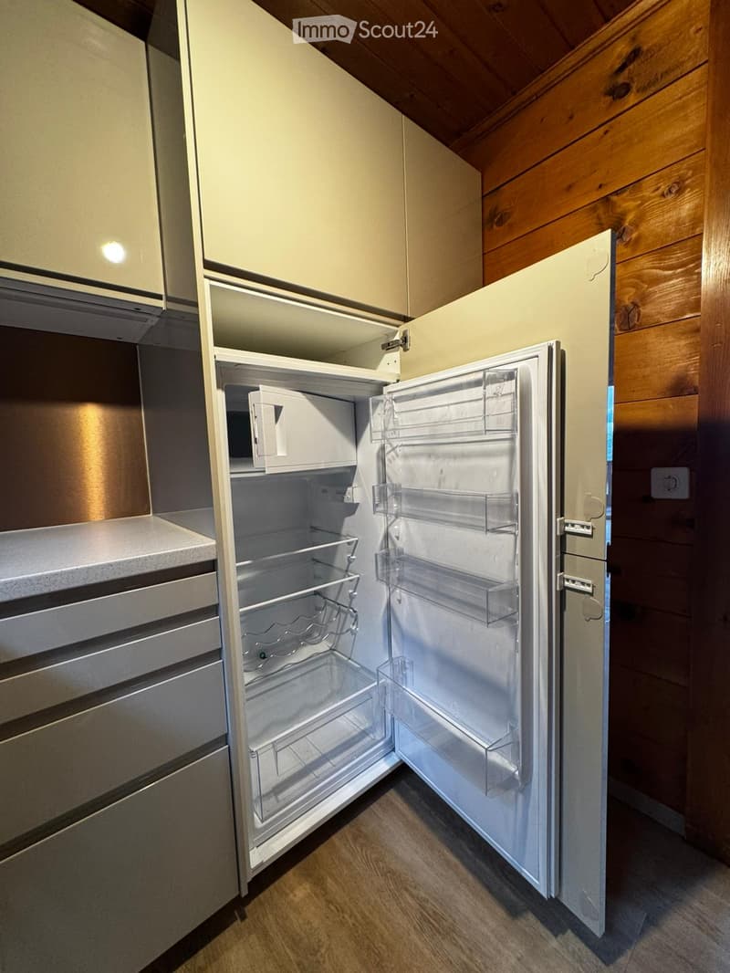 Open refrigerator with microwave, wooden wall, white cabinets, drawers, countertop