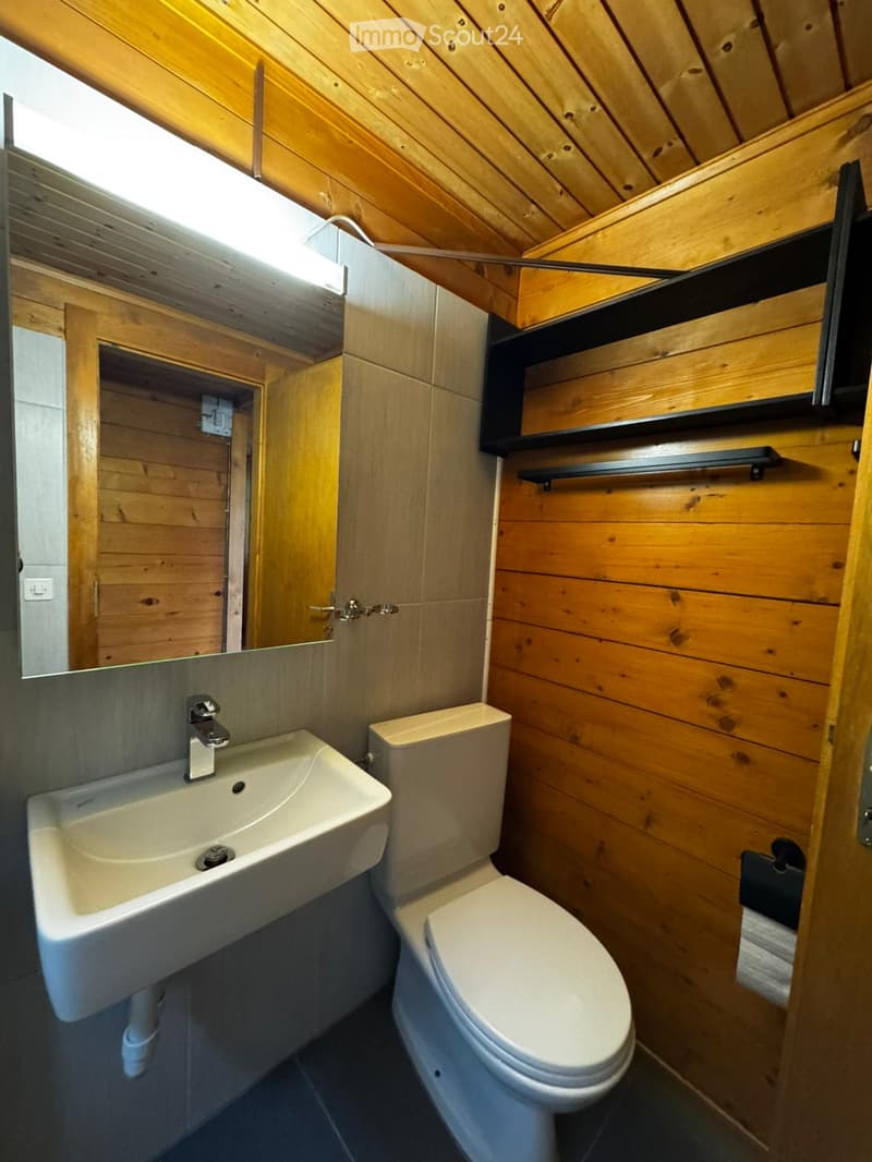 small bathroom with wooden walls, white sink, white toilet, mirror, toilet paper holder